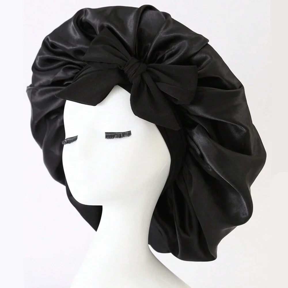 Black adjustable satin bonnet for sleeping with a large bow on a white mannequin head