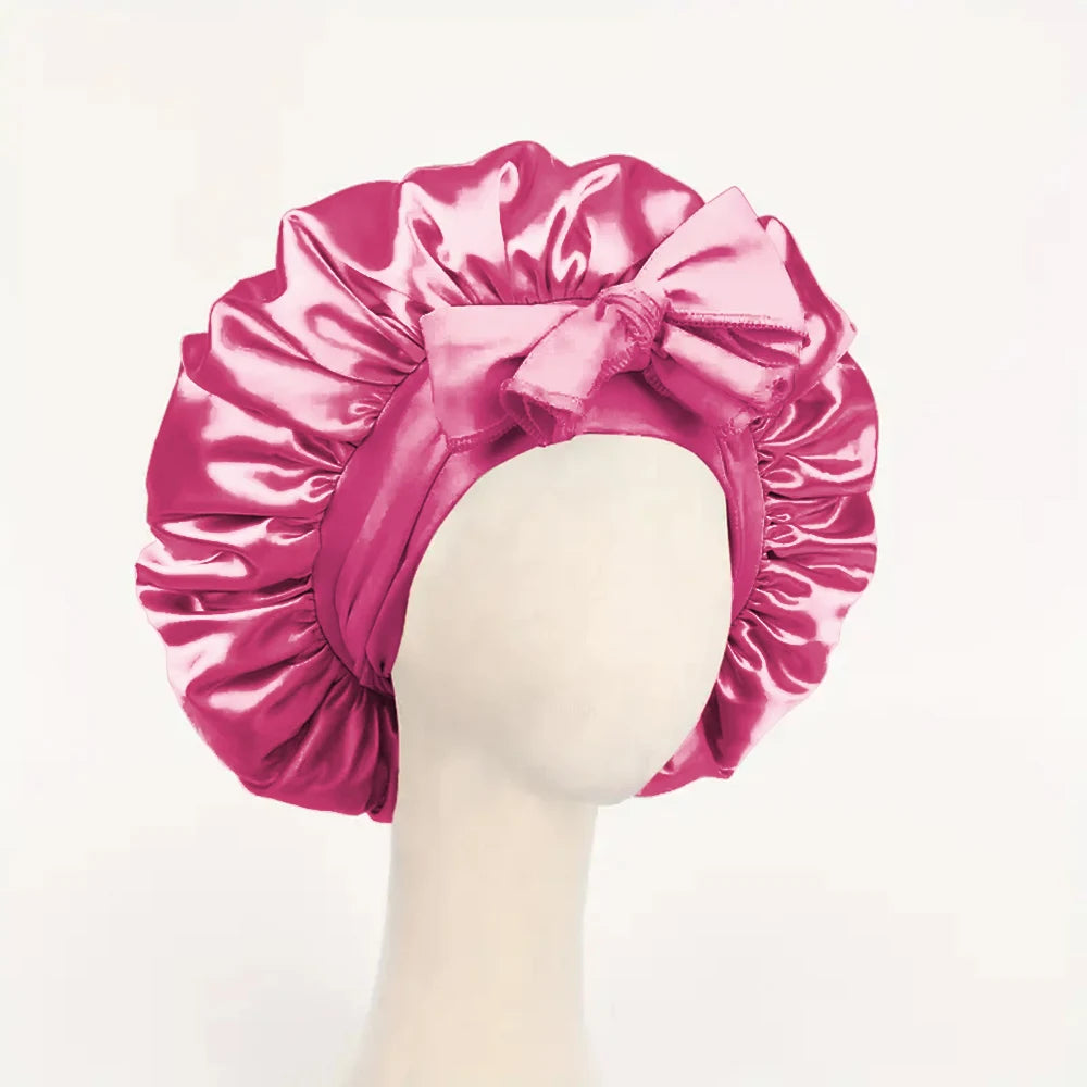 Pink adjustable satin bonnet for sleeping with a large decorative bow on a mannequin head