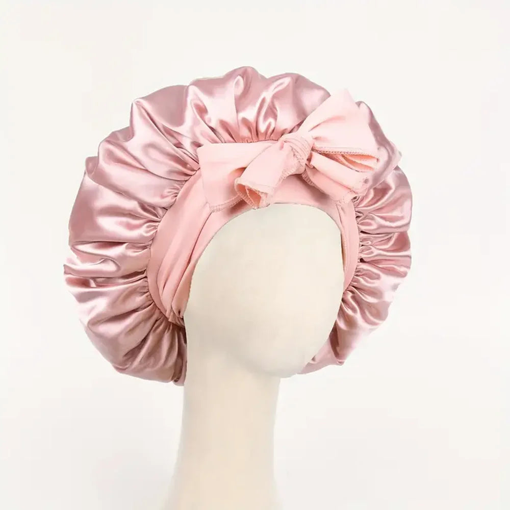 Pink adjustable satin bonnet for sleeping with a bow detail on a mannequin head