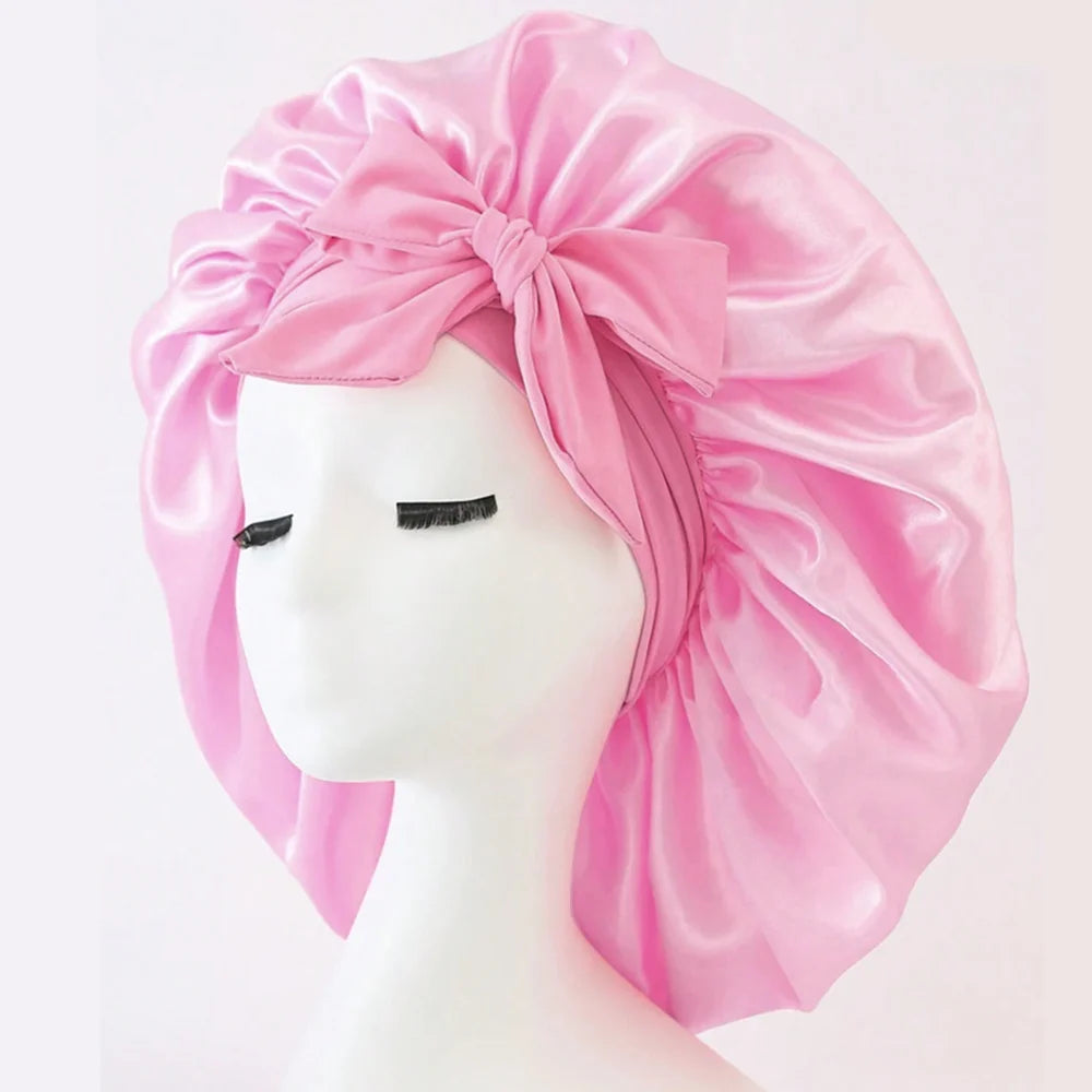 Pink adjustable satin bonnet for sleeping with large bow on white mannequin head by SACRED SELF WELLNESS
