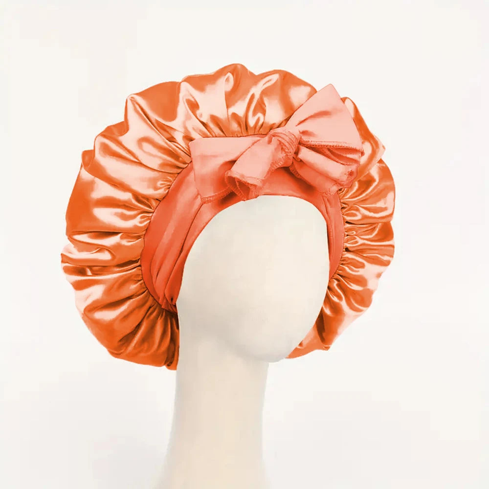 Orange adjustable satin bonnet for sleeping with a large bow detail on a mannequin head
