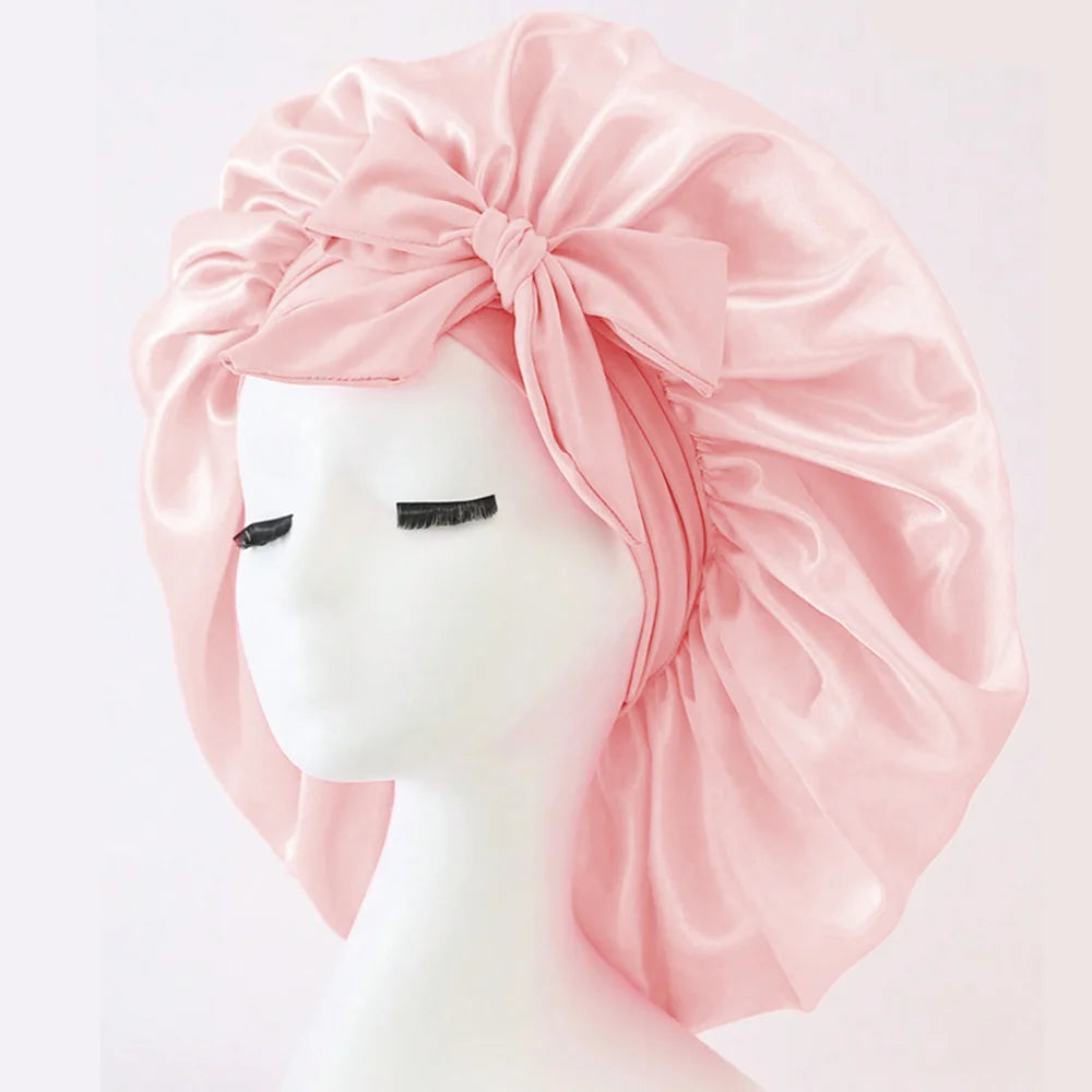 Pink adjustable satin bonnet for sleeping with a large bow on a white mannequin head