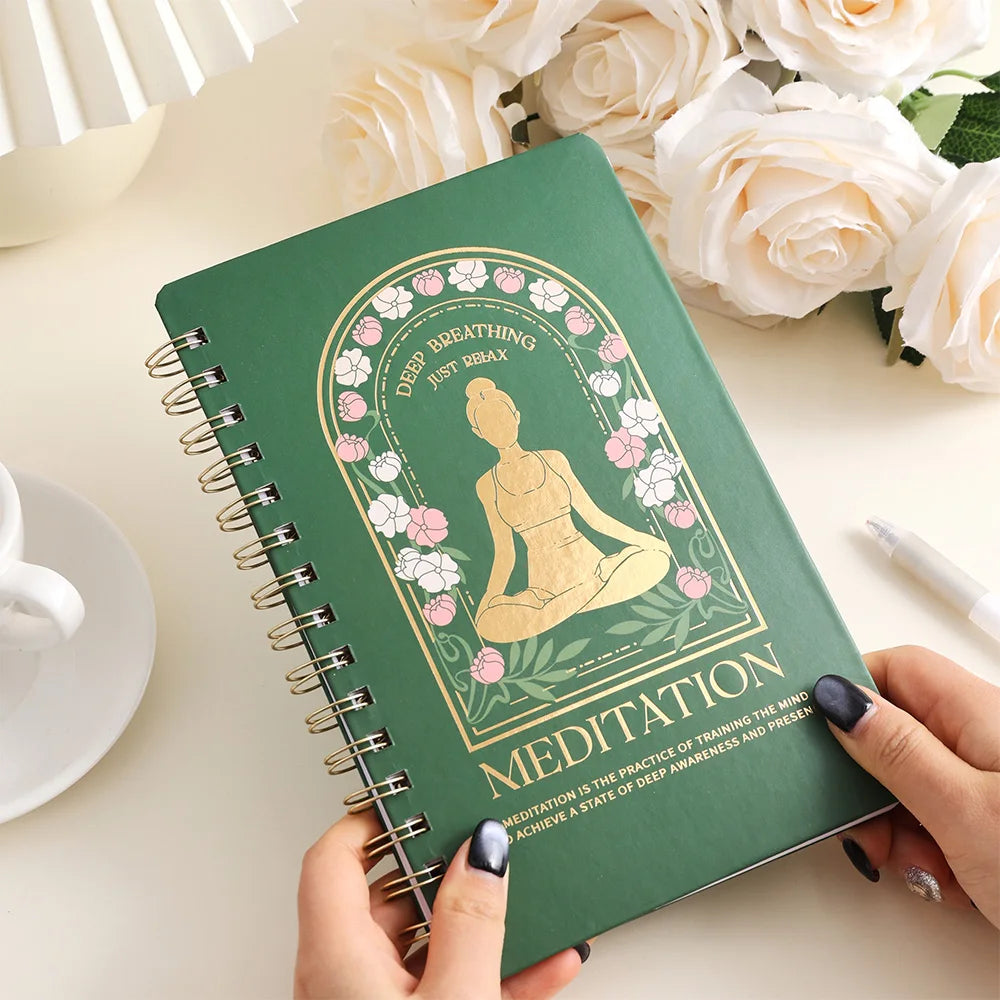 Meditation journal for mindfulness with green cover and floral design held by hands on white table
