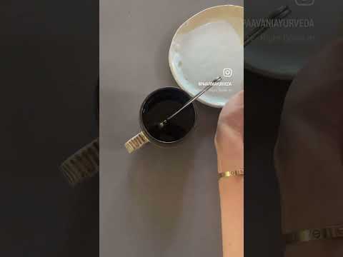 Hand stirring a cup of dark rooibos chai blend tea next to a white plate on a gray surface
