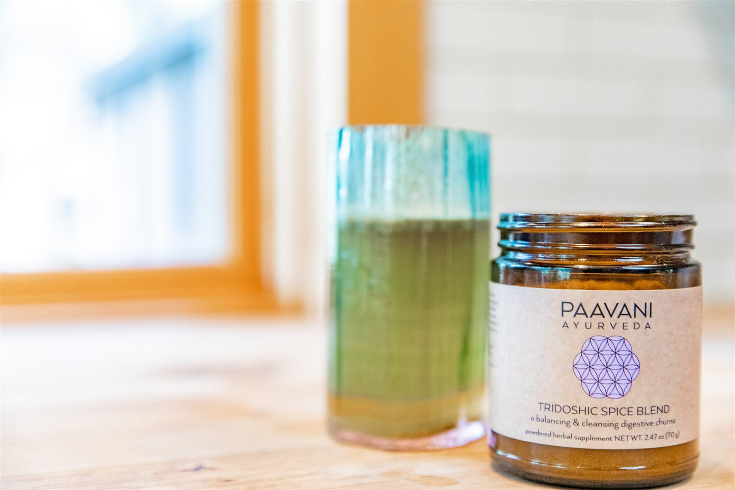 DC-PAAVANI Ayurveda tridoshic spice blend jar next to a green herbal drink on a wooden table