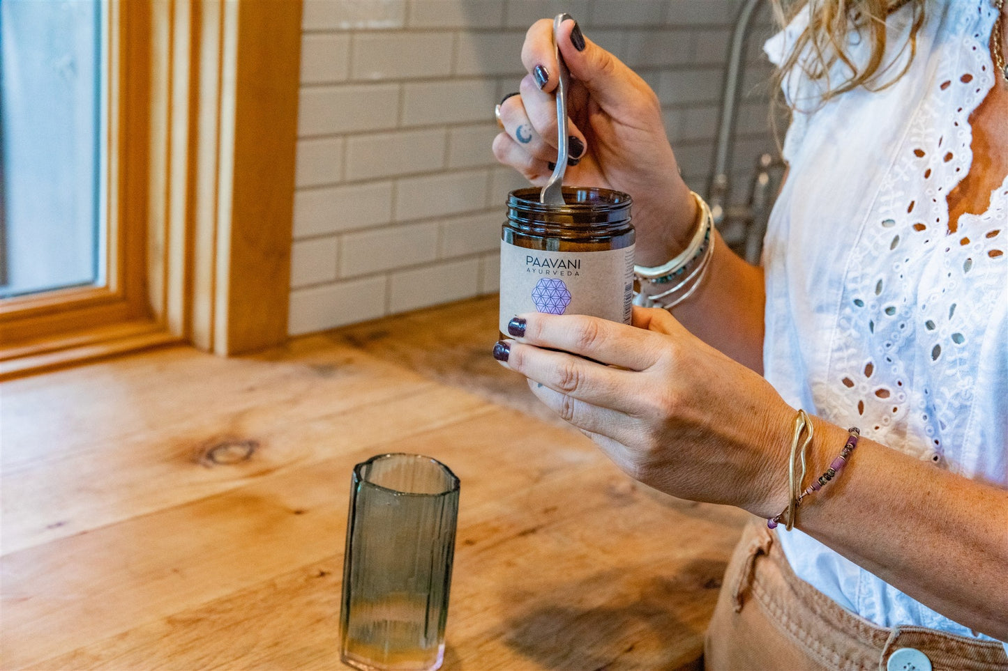 Person holding a jar of DC-PAAVANI Ayurveda tridoshic spice blend with a spoon over wooden countertop