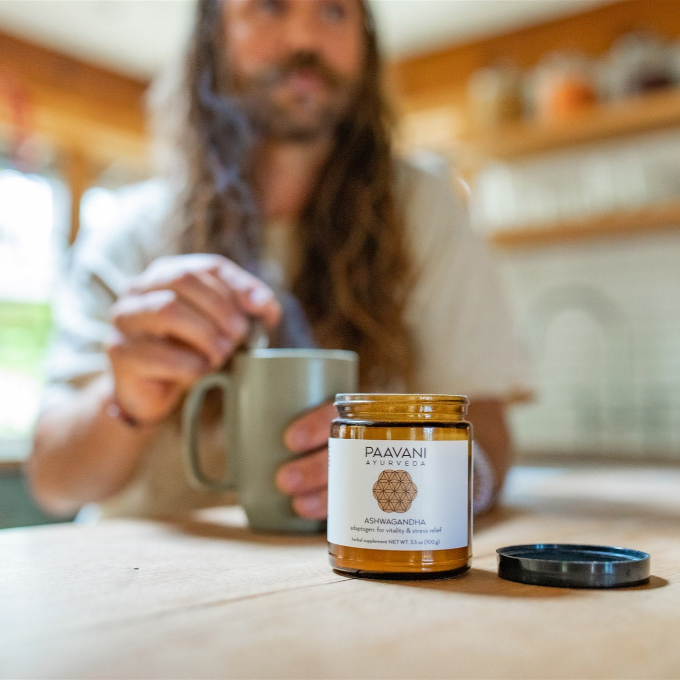 Paavani Ayurveda Ashwagandha jar with a man stirring a mug in the background Ayurvedic tonic for daily wellness