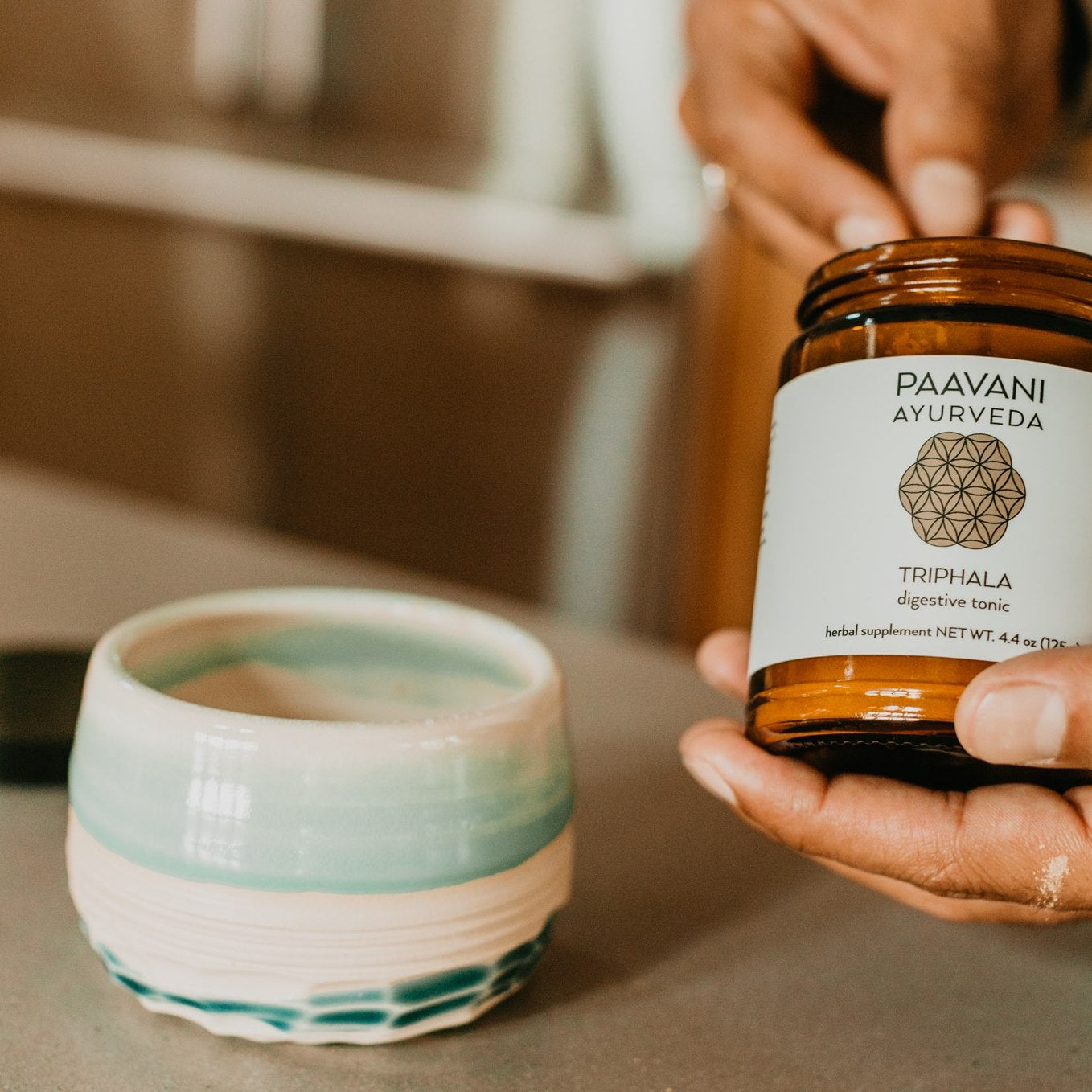 Paavani Ayurveda Triphala digestive tonic jar held near ceramic cup Ayurvedic tonic for daily wellness