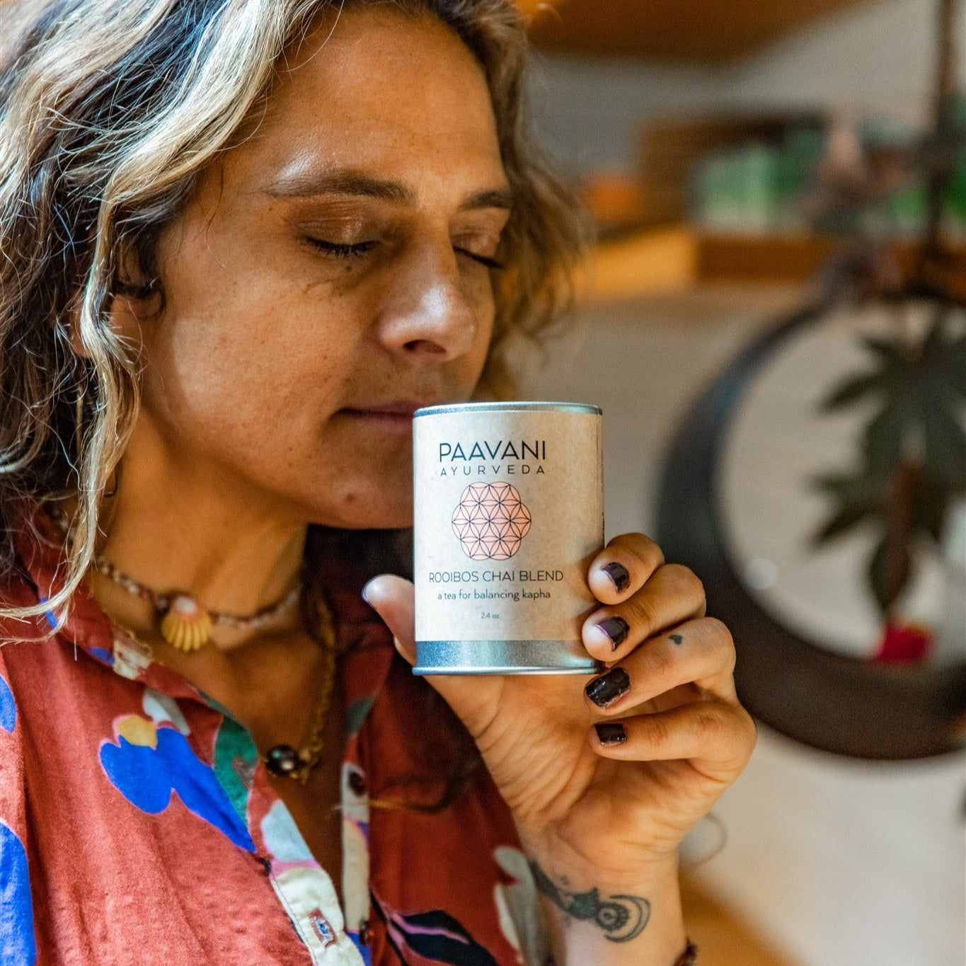 Woman holding a container of DC-PAAVANI Ayurveda rooibos chai blend tea with eyes closed