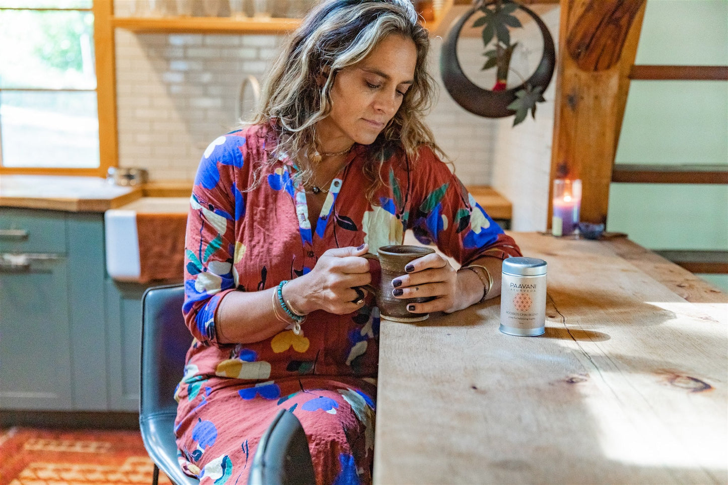 Woman enjoying a cup of tea from a herbal tea ritual set by DC-PAAVANI Ayurveda at a wooden kitchen table
