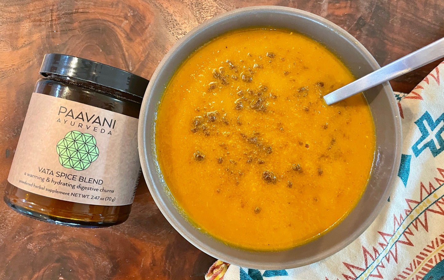 Vata spice blend for digestion jar by DC-PAAVANI Ayurveda next to a bowl of spiced soup with a spoon