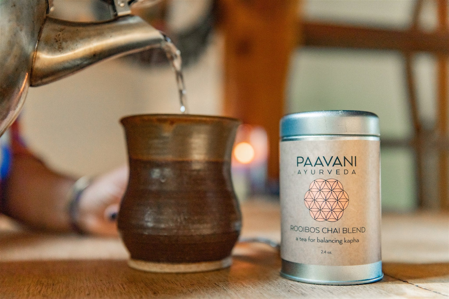 DC-PAAVANI Ayurveda rooibos chai blend tea tin next to a cup being poured from a kettle on a wooden table