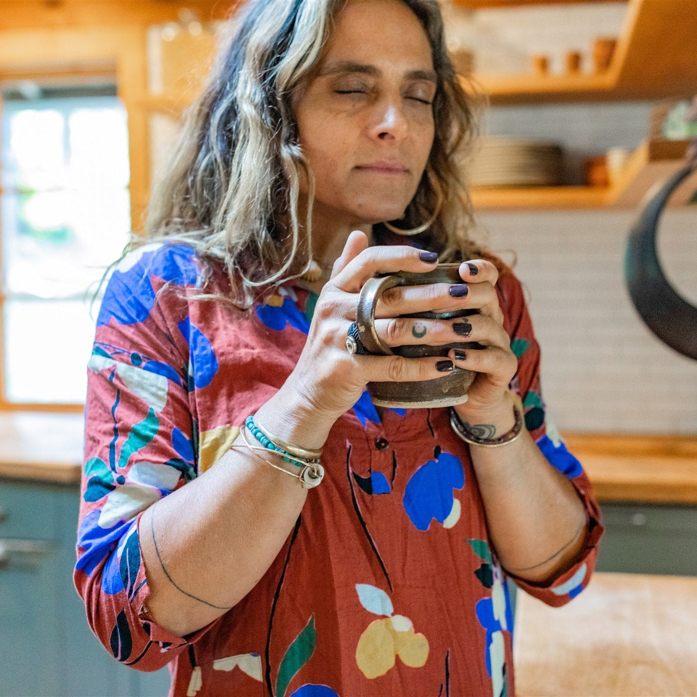 Woman enjoying a cup of rooibos chai blend tea in a cozy kitchen wearing a colorful floral dress