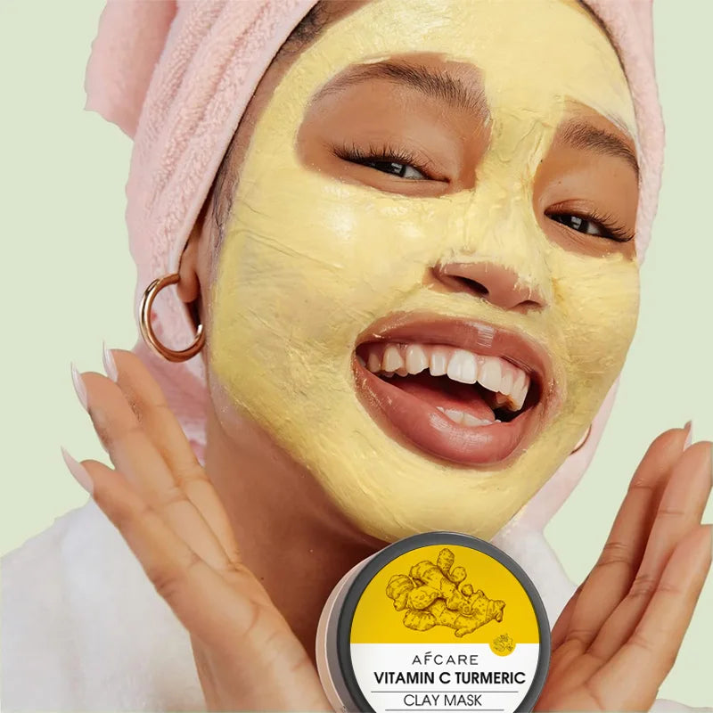 Smiling woman with yellow clay facial mask applied and holding vitamin c turmeric clay facial mask set