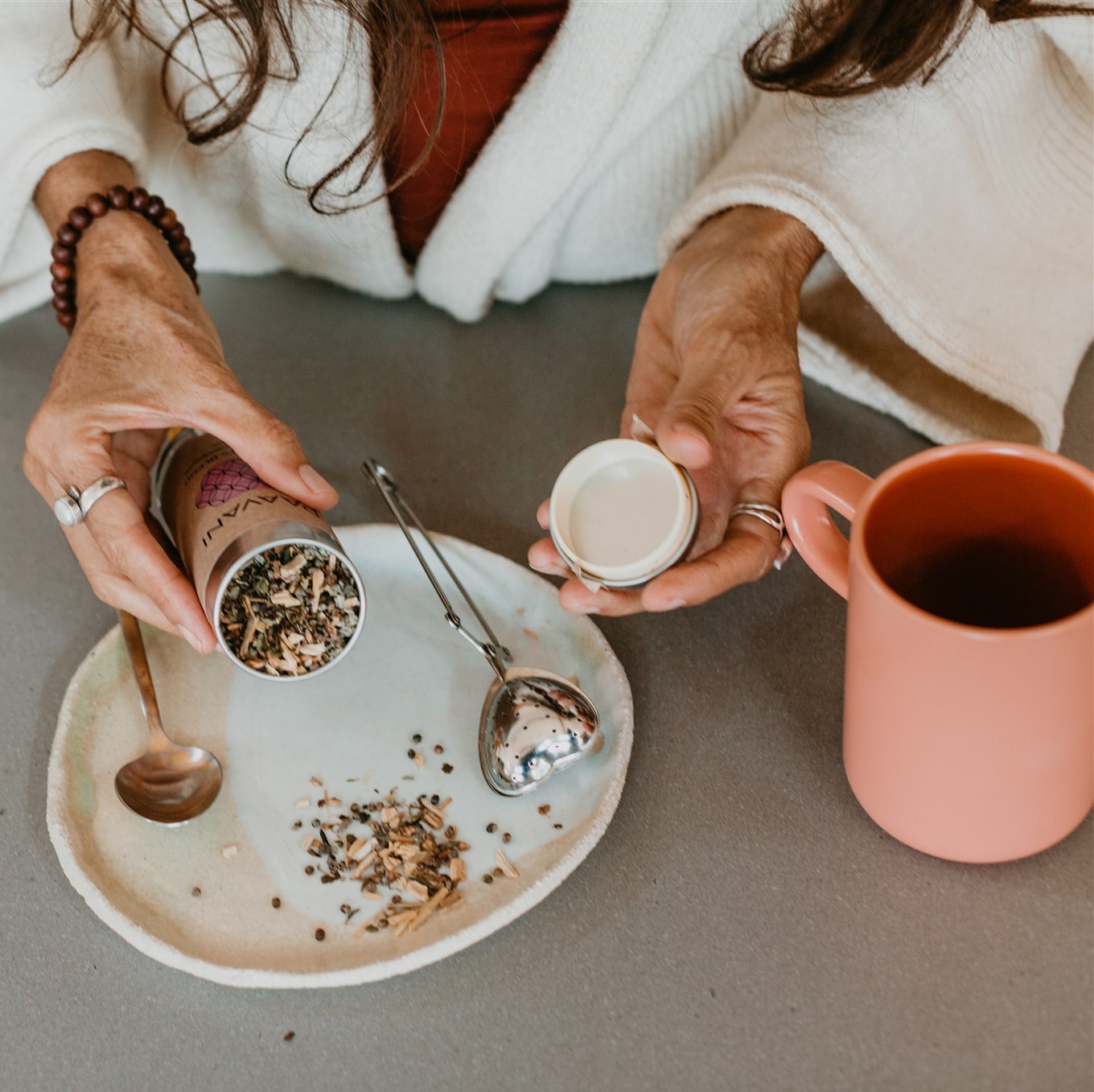 Hands preparing herbal tea with Ayurvedic herbs and a mug for Ayurvedic consultations online