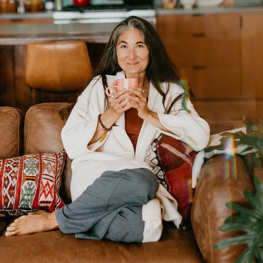 Smiling woman relaxing on couch holding a mug depicting Ayurvedic consultations online with comfort