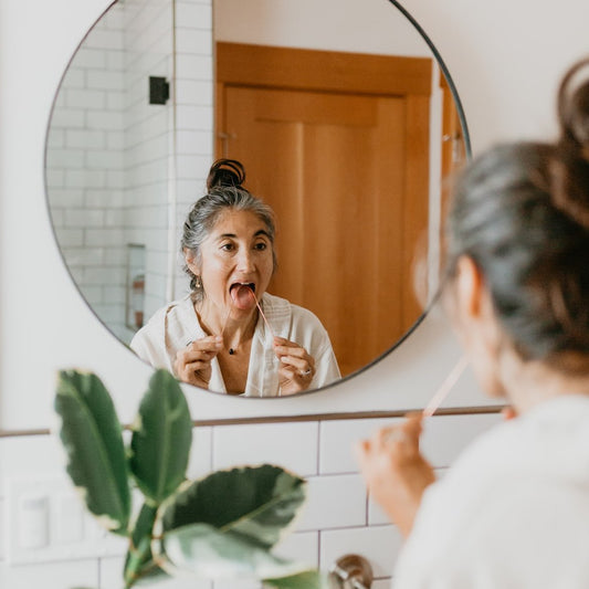 Woman practicing Ayurvedic daily routine class by tongue cleaning in front of bathroom mirror
