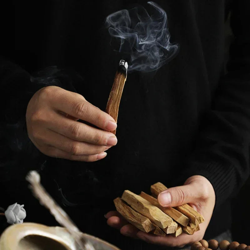 Person holding burning palo santo incense sticks with smoke and additional sticks in hand by Sacred Self Wellness