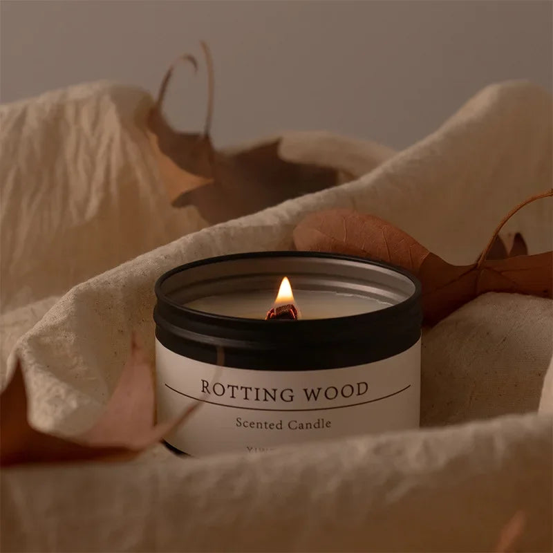 Scented candle with dried flowers labeled Rotting Wood burning on soft fabric background