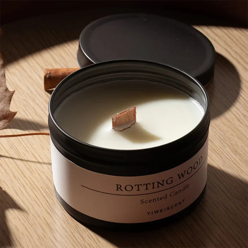 Scented candle with dried flowers in black container labeled Rotting Wood on wooden surface