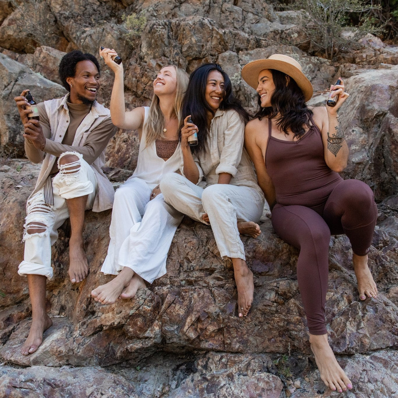 Group of diverse friends sitting on rocks enjoying Ayurvedic aromatherapy kit sprays in nature