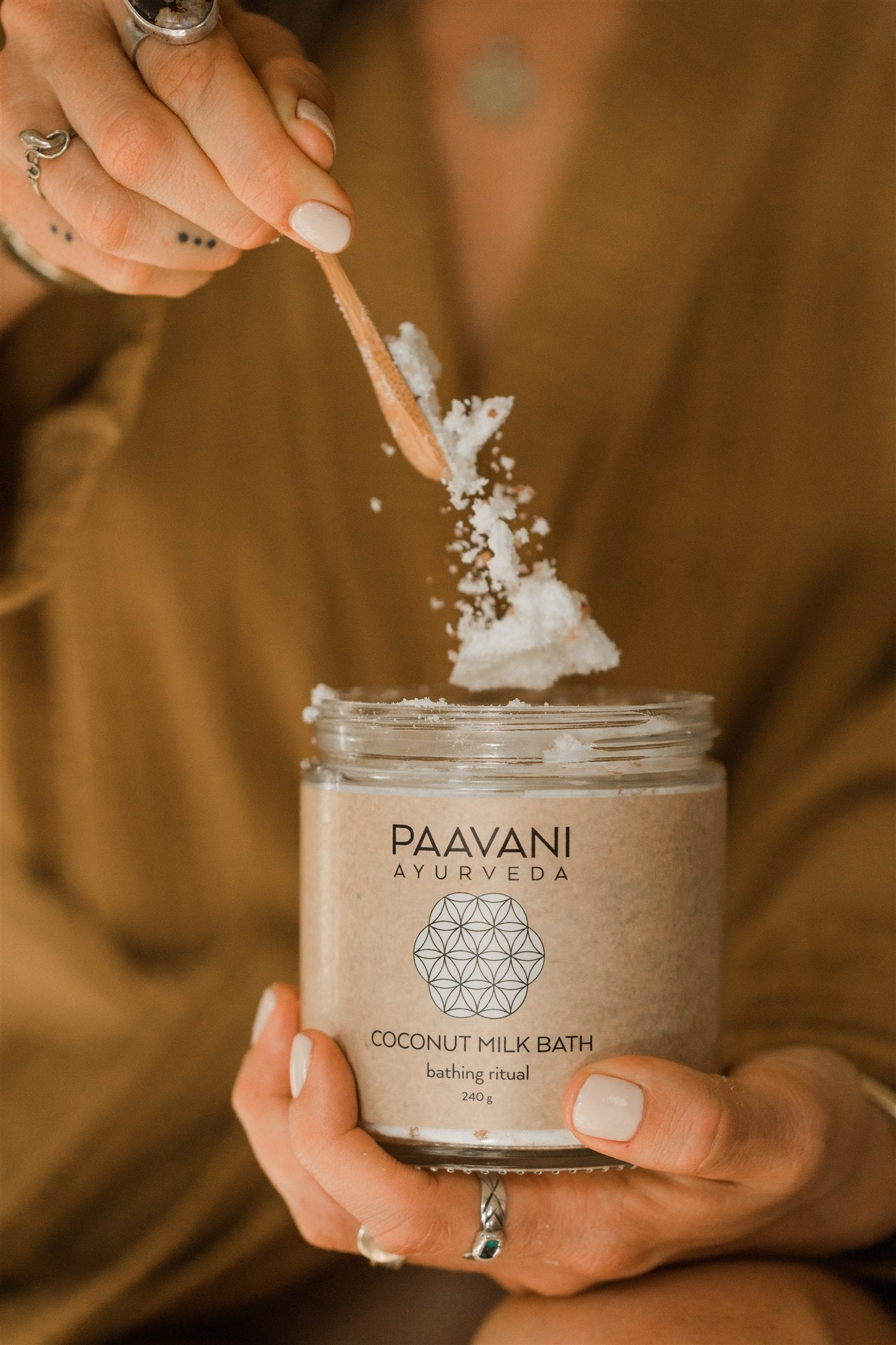 DC-PAAVANI Ayurveda Ayurvedic coconut milk bath powder in glass jar with wooden spoon held by hands