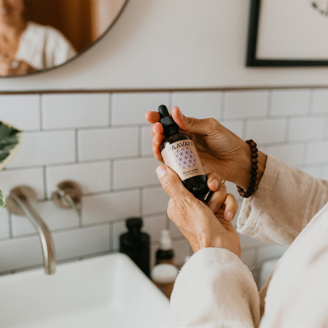 Person holding DC-PAAVANI Ayurveda botanical floral water for skin in a bathroom setting