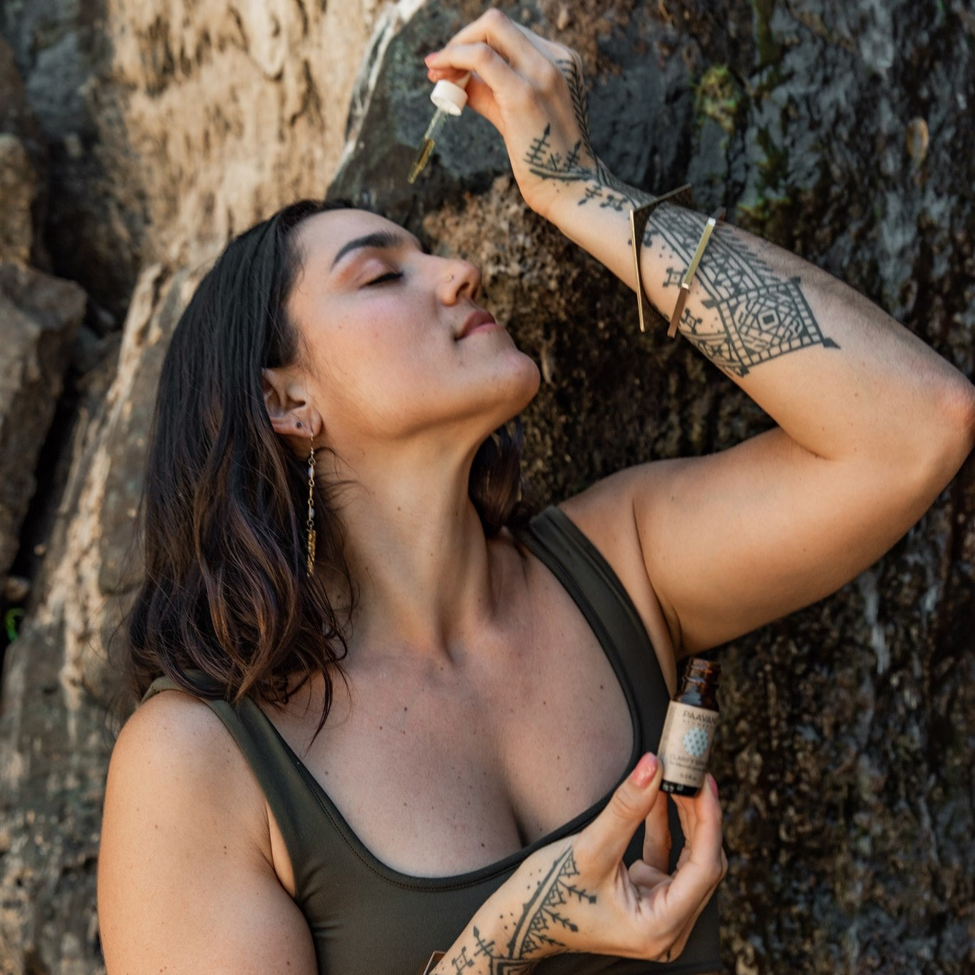 Woman applying clarifying facial ritual for acne serum from dropper bottle near rock wall