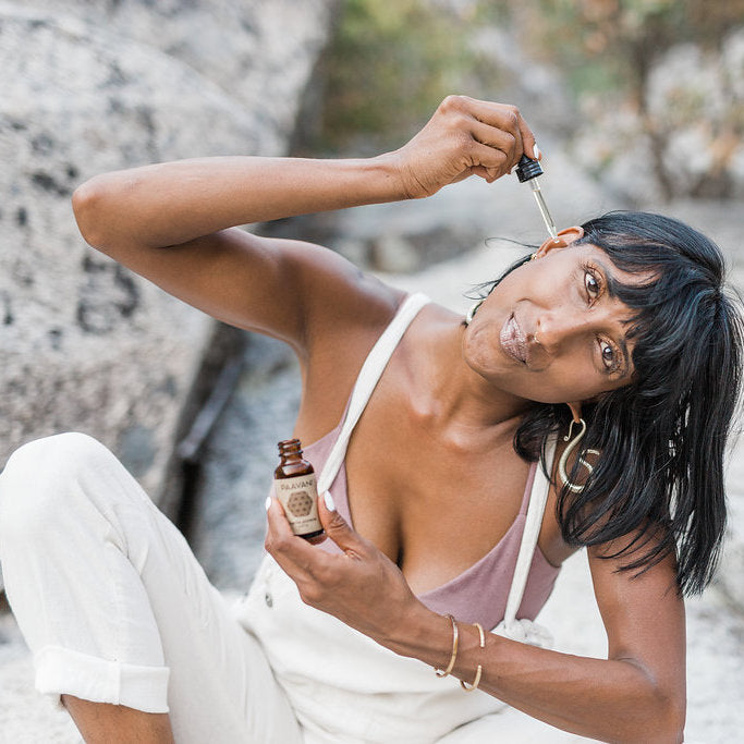 Woman using oil from Dinacharya ritual kit for daily wellness in an outdoor natural setting