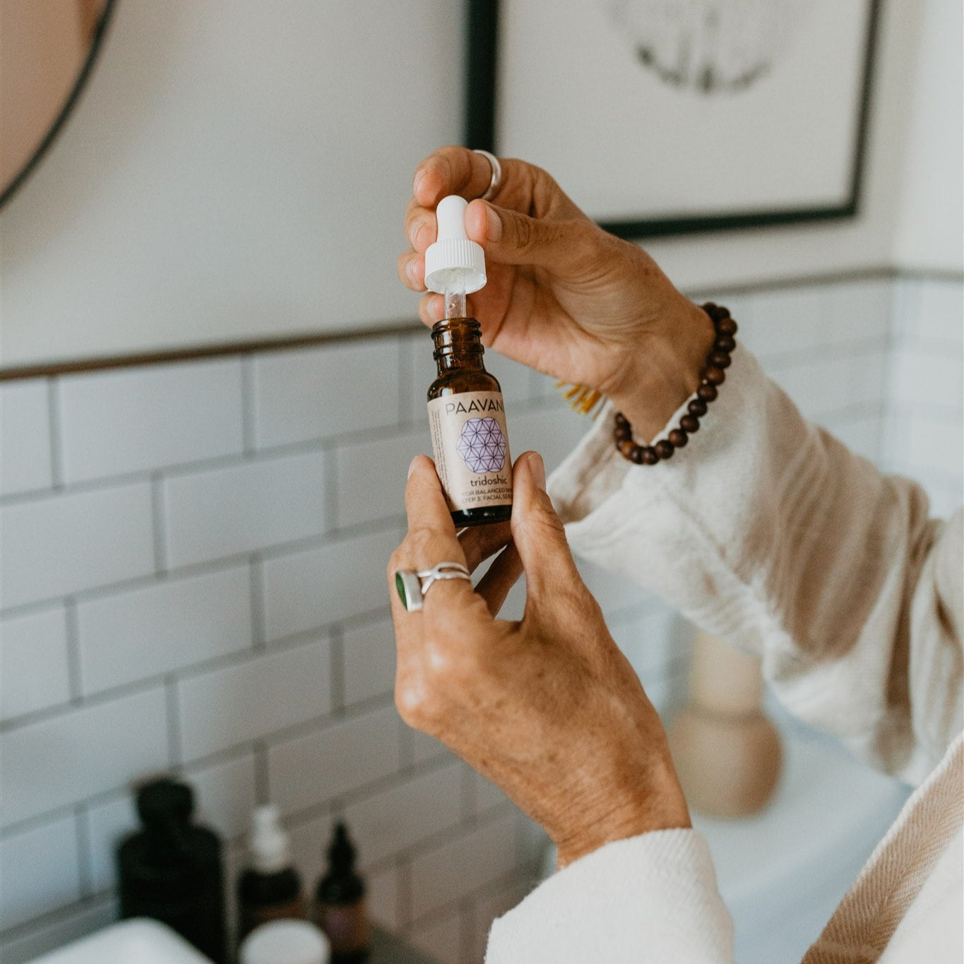 Person holding DC-PAAVANI Ayurveda serum dropper bottle from the tridoshic facial ritual kit in a bathroom