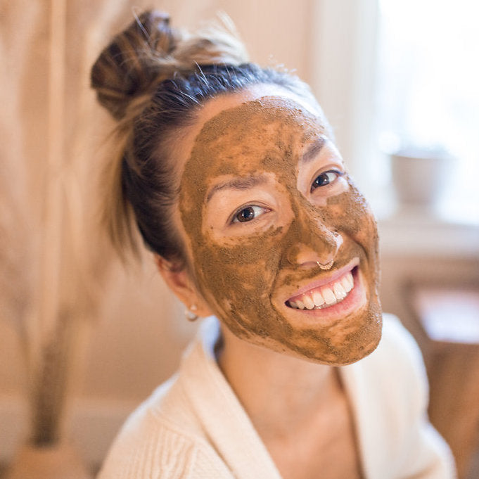 Smiling woman with a natural brown facial mask applied using the vata facial ritual set by DC-PAAVANI Ayurveda