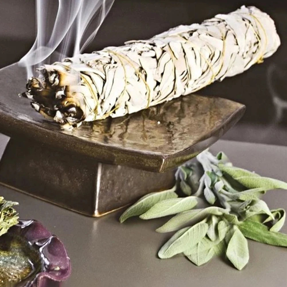 SACRED SELF WELLNESS palo santo white sage smudge stick emitting smoke on a bronze holder with fresh sage leaves nearby